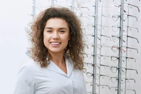 Ophtalmologiste bouclé souriant posant près du stand avec des lunettes . — Photo