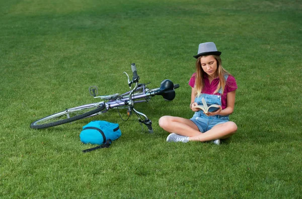 Junges Mädchen sitzt neben Fahrrad auf Gras. — Stockfoto