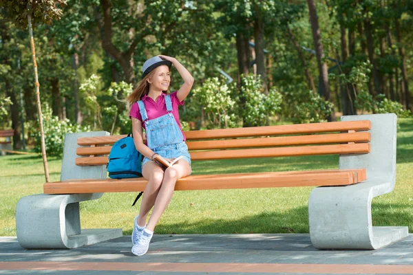 本の保管のベンチに座っているスタイリッシュな服を着た少女. — ストック写真