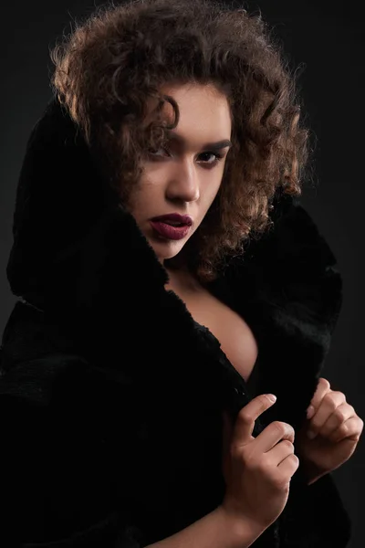 Portré szenvedélyes göndör lány pózol fekete kabát. — Stock Fotó