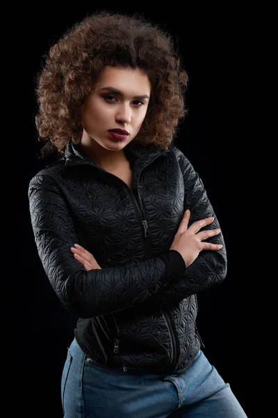 Confident curly girl wearing black jacket and blue jeans.