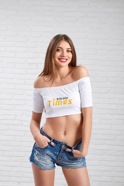 Smiling sporty beautiful female model in denim shorts and white crop top with bitcoin logo — Stock Photo, Image