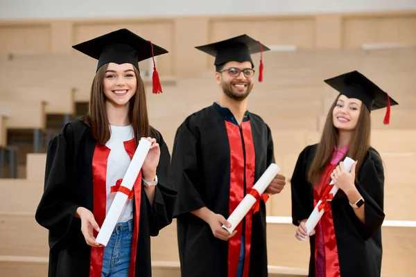 Graduados sorridentes mantendo diplomas na frente de mesas de madeira . — Fotografia de Stock