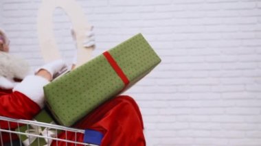 Noel Baba hediye kutularıyla alışveriş arabasının içinde yatıyor.