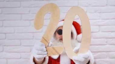 Güneş gözlüklü yaşlı Noel Baba 2 ve 0 tahta parmaklar gösteriyor.