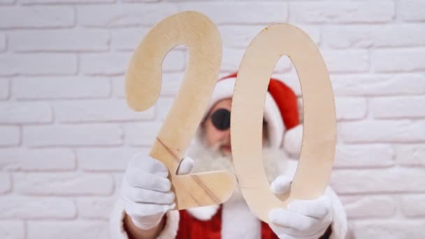 Gealterter Weihnachtsmann mit Sonnenbrille, der 2 und 0 Holzzahlen zeigt — Stockvideo