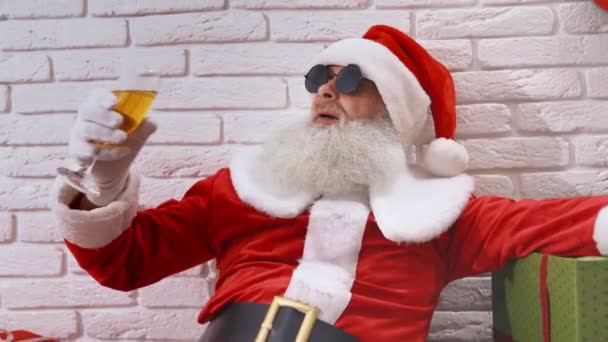 Güneş gözlüklü mutlu Noel Baba köpüklü şarabın tadını çıkarıyor. — Stok video