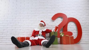 Komik yaşlı Noel Baba, duvarın yanında dinleniyor ve soda içiyor.