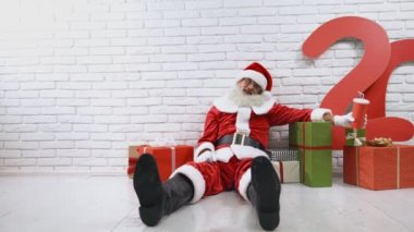 Noel Baba kostümlü yaşlı bir adam stüdyoda hediye kutularıyla oturuyor.
