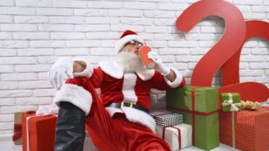 Olgun Noel Baba yerde kırmızı bardaktan soda içiyor.