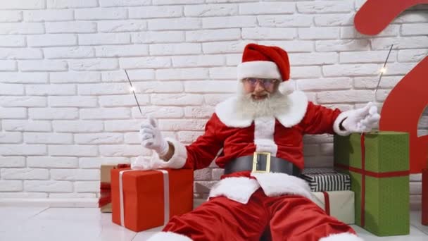 Feliz anciano Papá Noel sentado en el suelo con destellos — Vídeos de Stock