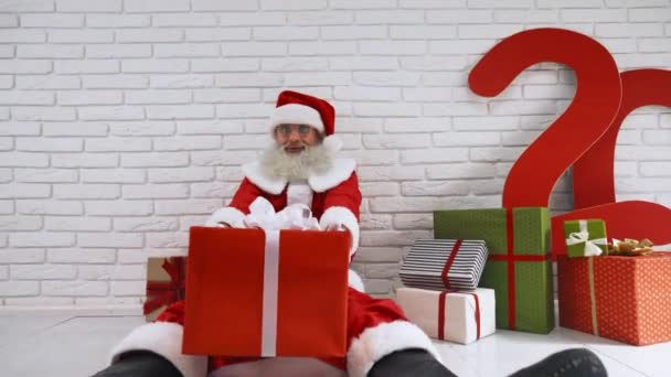 Noel Baba kostümlü, yerde hediye kutuları olan neşeli yaşlı bir adam. — Stok video