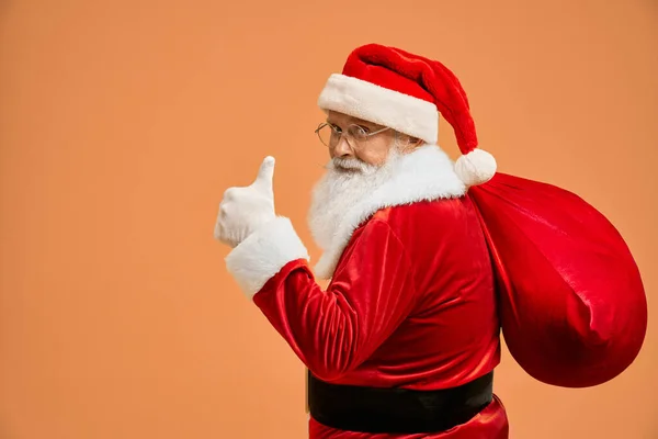 Dojrzałe Santa Claus niesie duży czerwony worek i pokazuje kciuk w górę — Zdjęcie stockowe