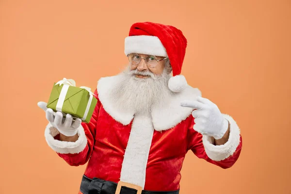 Starzejący się Święty Mikołaj patrząc w kamerę i wskazując na pudełko prezentów — Zdjęcie stockowe