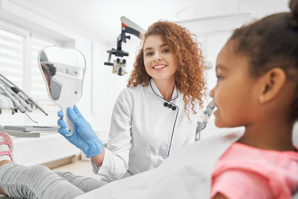 Dentista sosteniendo espejo en forma de diente para niña . — Foto de Stock