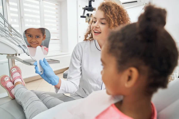 Liten flicka tittar på spegel i form av tand. — Stockfoto