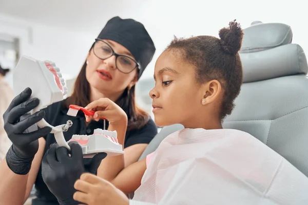 Dentista enseñando a chica a cepillarse los dientes . — Foto de Stock