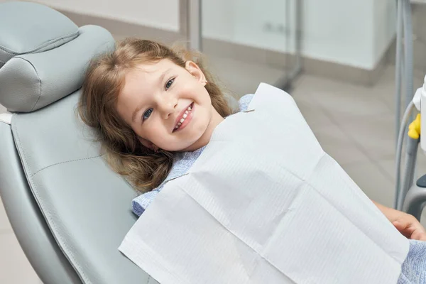 Sonriendo lindo, niño pequeño sentado en la silla dental . — Foto de Stock