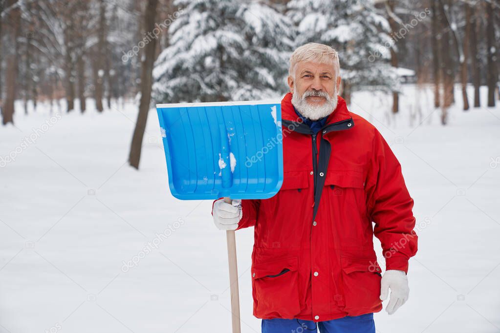 Elderly cleaner posing with shovel outdoors