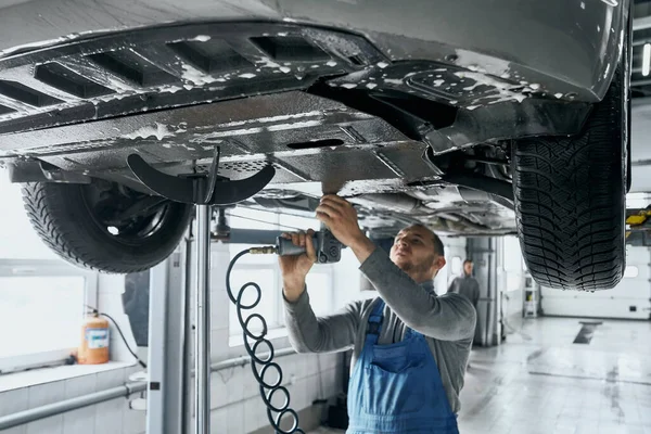Fachkundiger Mechaniker in blauen Overalls repariert Autoaufhängung — Stockfoto