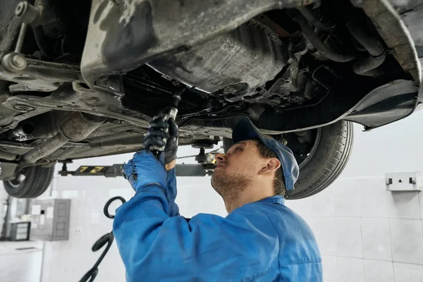 Profesionální mechanik pracující s nástroji pod zdviženým vozem — Stock fotografie