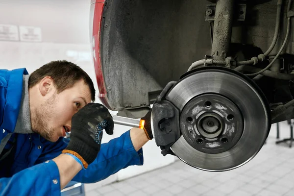 Male mechanic holding flashlight and examining brake pads — Stock Photo, Image