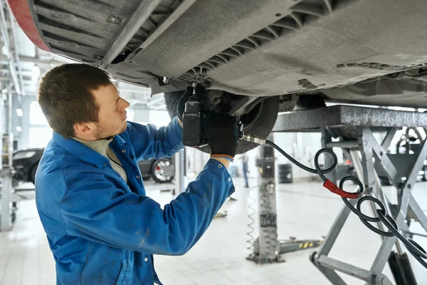 Ein männlicher Spezialist repariert das Gerät unter dem Auto in der Garage — Stockfoto