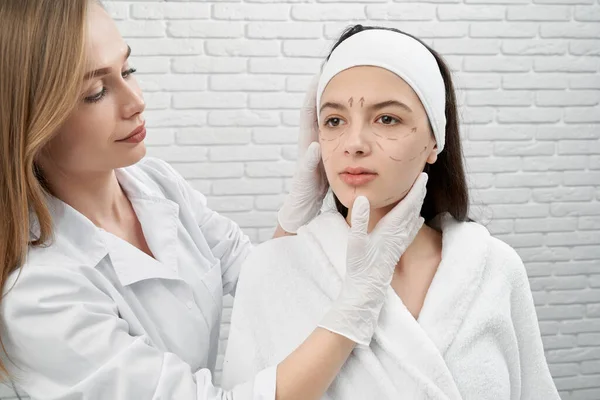 Esteticista y mujer con líneas negras para corrección . — Foto de Stock