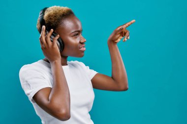 Kısa saçlı Afro kadın kulaklıklı müzik dinliyor.