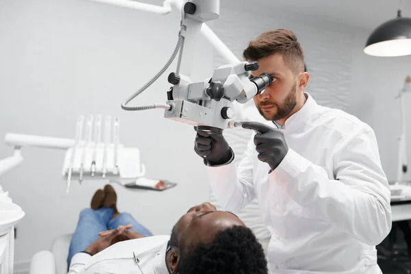 Odontólogo masculino examinando dientes de paciente masculino en clínica —  Fotos de Stock