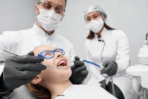 Chica acostada en la silla del dentista mientras el médico cura los dientes — Foto de Stock