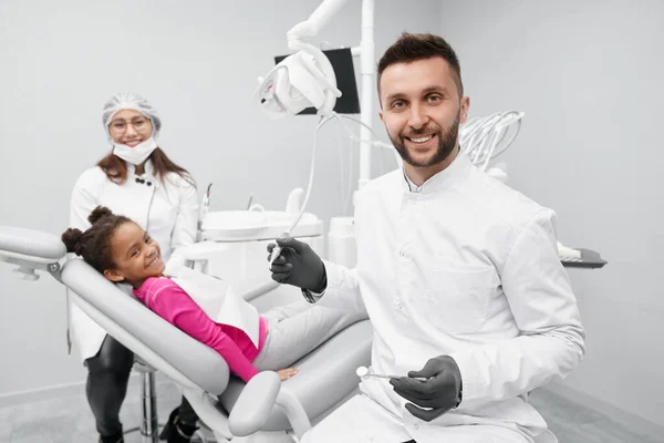 Dentista tenere attrezzature mentre il bambino sdraiato sulla sedia del dentista — Foto Stock