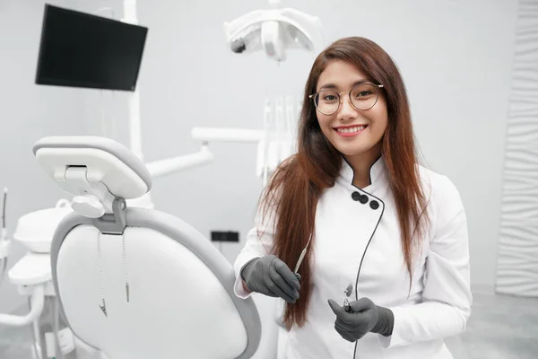Dentista che tiene strumenti dentali e sorride in clinica — Foto Stock