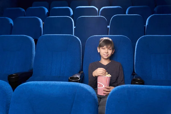 Piccolo spettatore maschio seduto da solo nel cinema e sorridente — Foto Stock