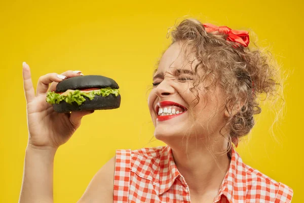 Porträt eines lächelnden fröhlichen blonden Mädchens, das schwarzen Burger isst — Stockfoto