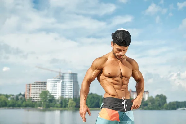 Deportista con torso desnudo mostrando músculos cerca del lago . — Foto de Stock