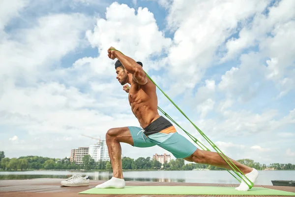 Hombre fuerte haciendo estiramiento, entrenamiento cerca del lago . — Foto de Stock