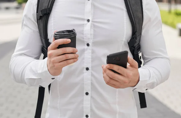 Hombre con mochila sosteniendo teléfono negro y taza de café . — Foto de Stock