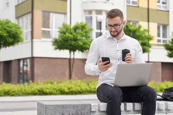 IT worker sitting on bench, looking at phone.