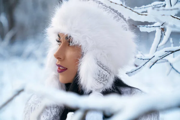 Дівчина в теплому зимовому капелюсі біля гілок дерев зі снігом . — стокове фото