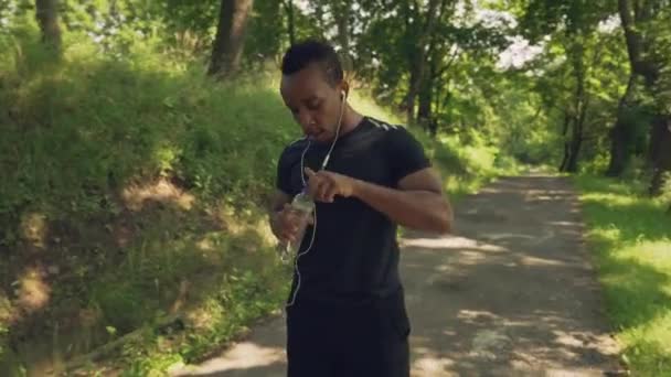 Mann trinkt Wasser und hört Musik beim Morgenlauf — Stockvideo