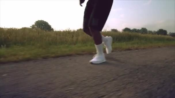 Ισχυρός άνδρας με σορτς και αθλητικά παπούτσια τρέχει ανάμεσα σε πράσινο πεδίο — Αρχείο Βίντεο