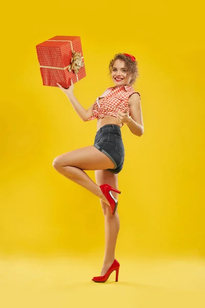 Lady standing on one leg holding red box with golden bow.