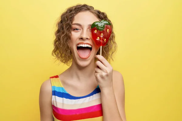 Chica feliz ocultando el ojo detrás de caramelo de baya piruleta . —  Fotos de Stock