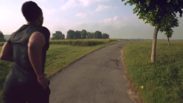 Vista posterior de un joven deportista afro corriendo sobre la naturaleza — Vídeos de Stock