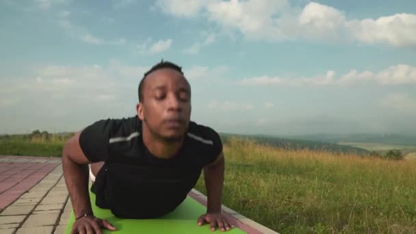 Atlético afro homem alongamento torso até no tapete de ioga na natureza — Vídeo de Stock