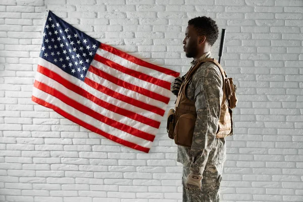 Vista lateral do soldado americano perto da bandeira nacional . — Fotografia de Stock