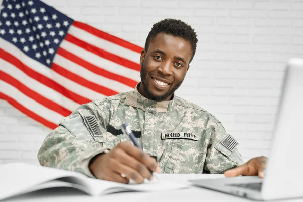 Happy soldier sitting on workplace and writing in documents.