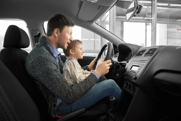 Funny daddy and son sitting on seat of drivers in new auto — Stockfoto