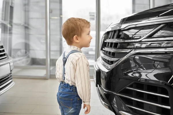 Вид сбоку на маленького мальчика, смотрящего на бампер большой черной машины — стоковое фото